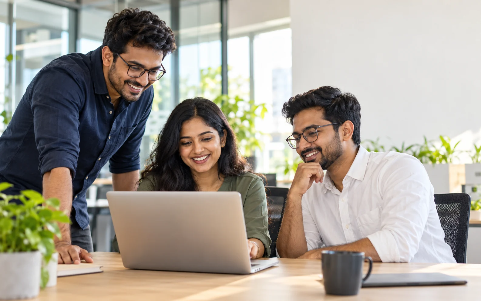 Three smiling colleagues sharing ideas around a laptop in a bright office