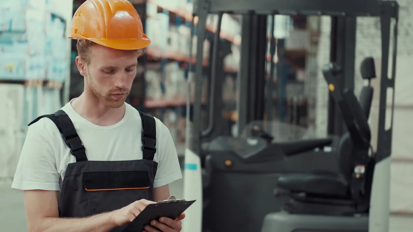 A warehouse professional wearing a safety helmet and reviewing a clipboard